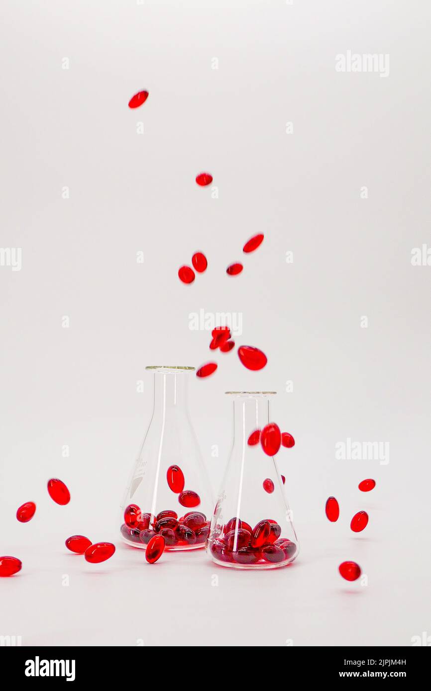 Capsule rosse di olio di krill in palloni da laboratorio su fondo bianco.omega naturale tre acidi.Fonte di acidi grassi omega 3. Capsule rosse volanti krill Foto Stock
