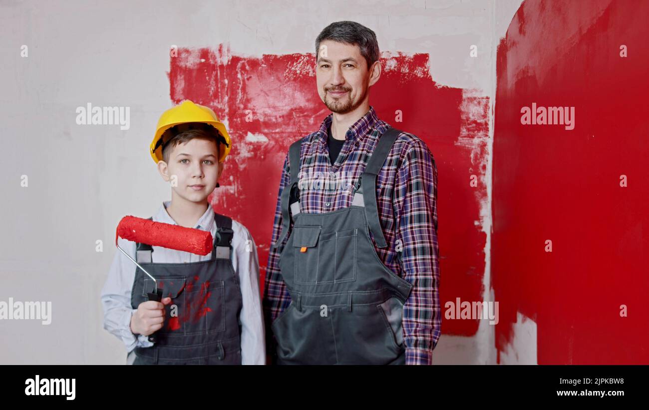 Un ragazzino e suo padre in piedi nella stanza e tenendo i rulli per la pittura a muro. Scatto medio Foto Stock