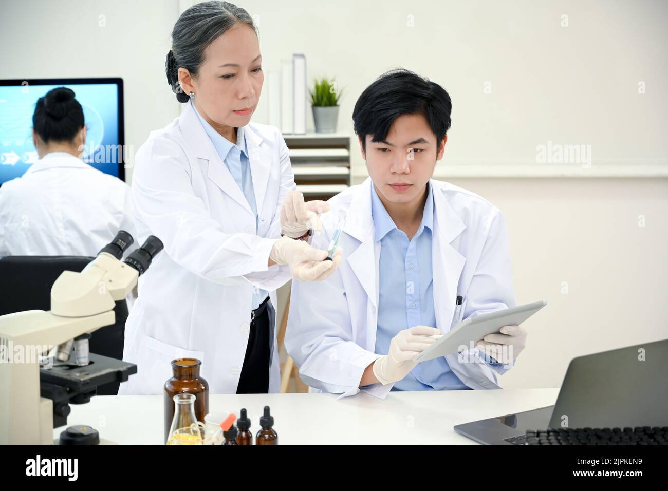 Due scienziati asiatici professionisti in cappotto bianco concentrandosi facendo un esperimento chimico, lavorando insieme nel laboratorio. Foto Stock