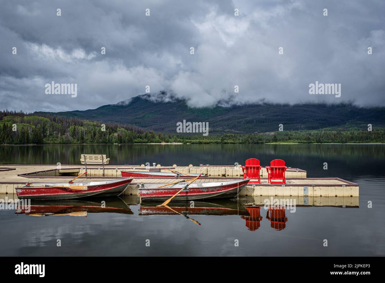 Nuvole basse in una mattinata ferma al lago Pyramid, il Jasper National Park attracca con barche e sedie rosse Foto Stock