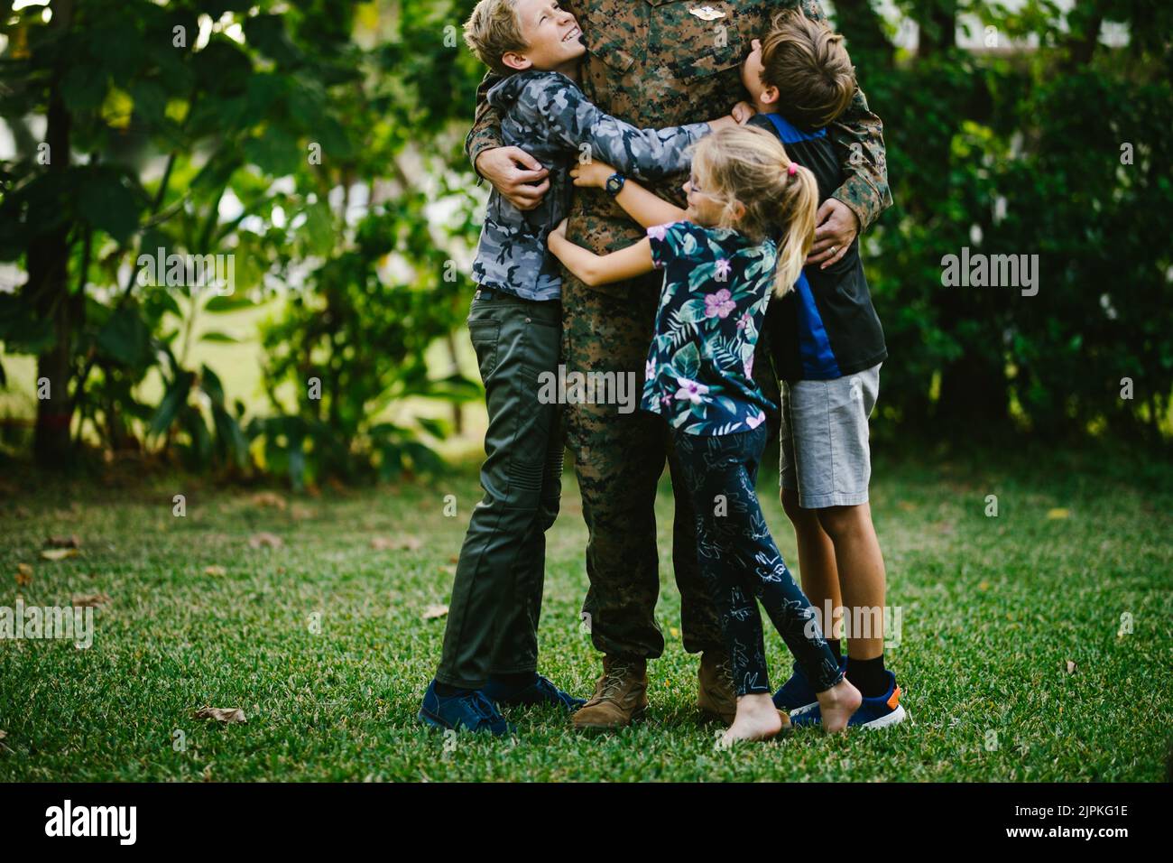 Tre bambini abbracciano il padre del membro del servizio dopo l'implementazione Foto Stock