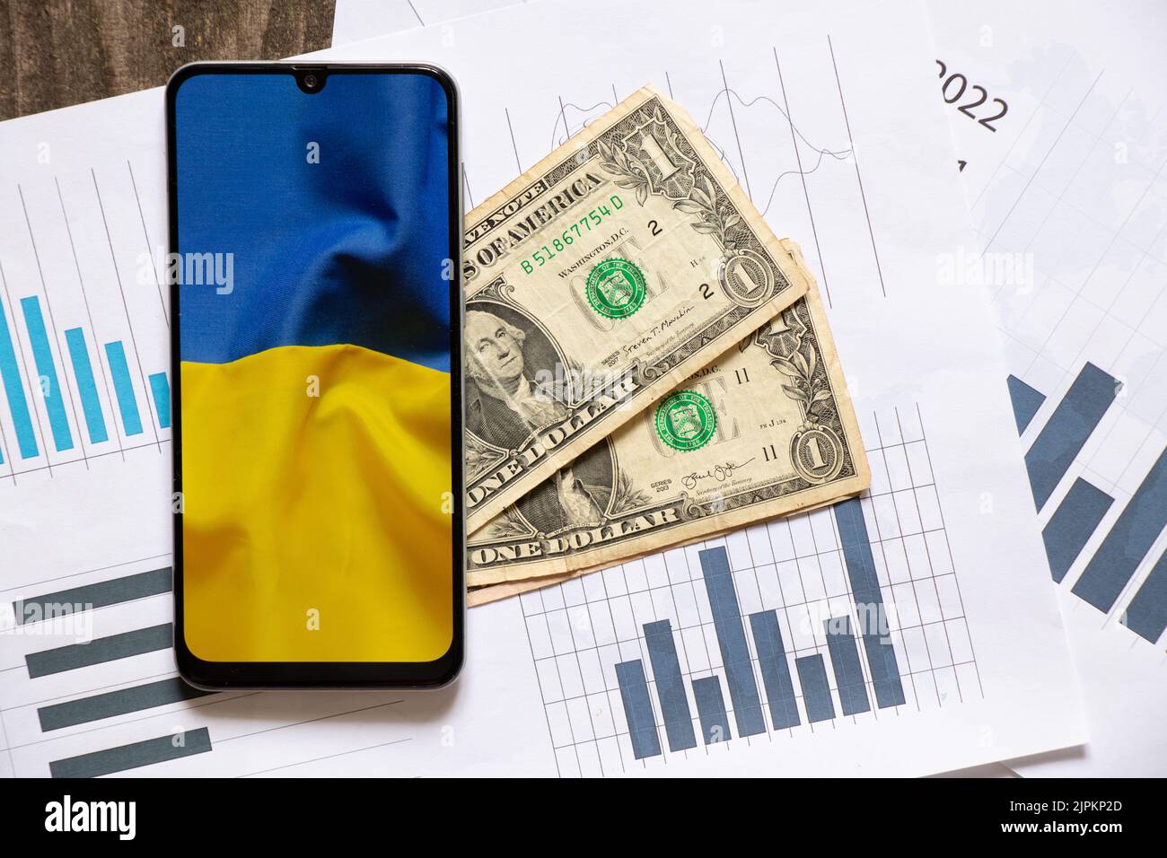 Un telefono con una foto della bandiera dell'Ucraina si trova su dollari e grafici a barre con i rapporti, l'economia in Ucraina, dollari e investimenti in Ucraina Foto Stock