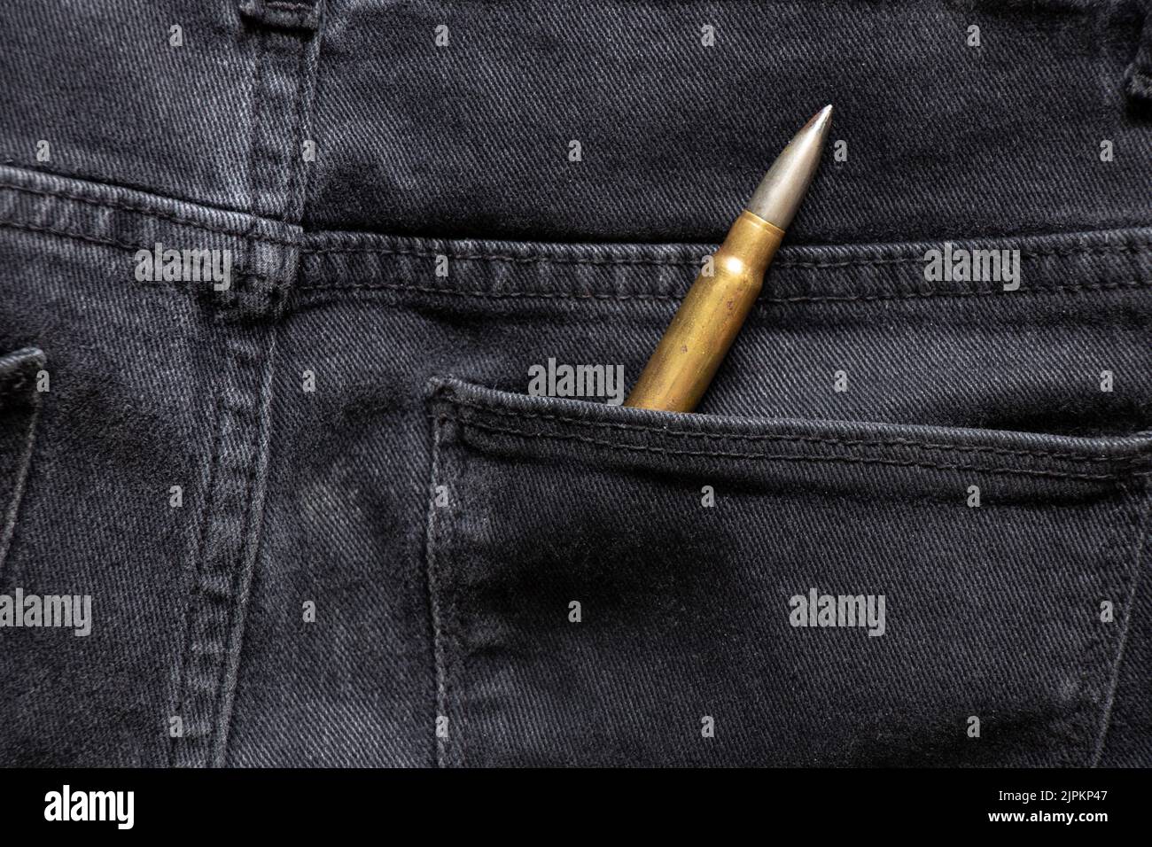 Proiettile militare in tasca di jeans grigi, arma per la protezione, tendenza alla moda, proiettile Foto Stock