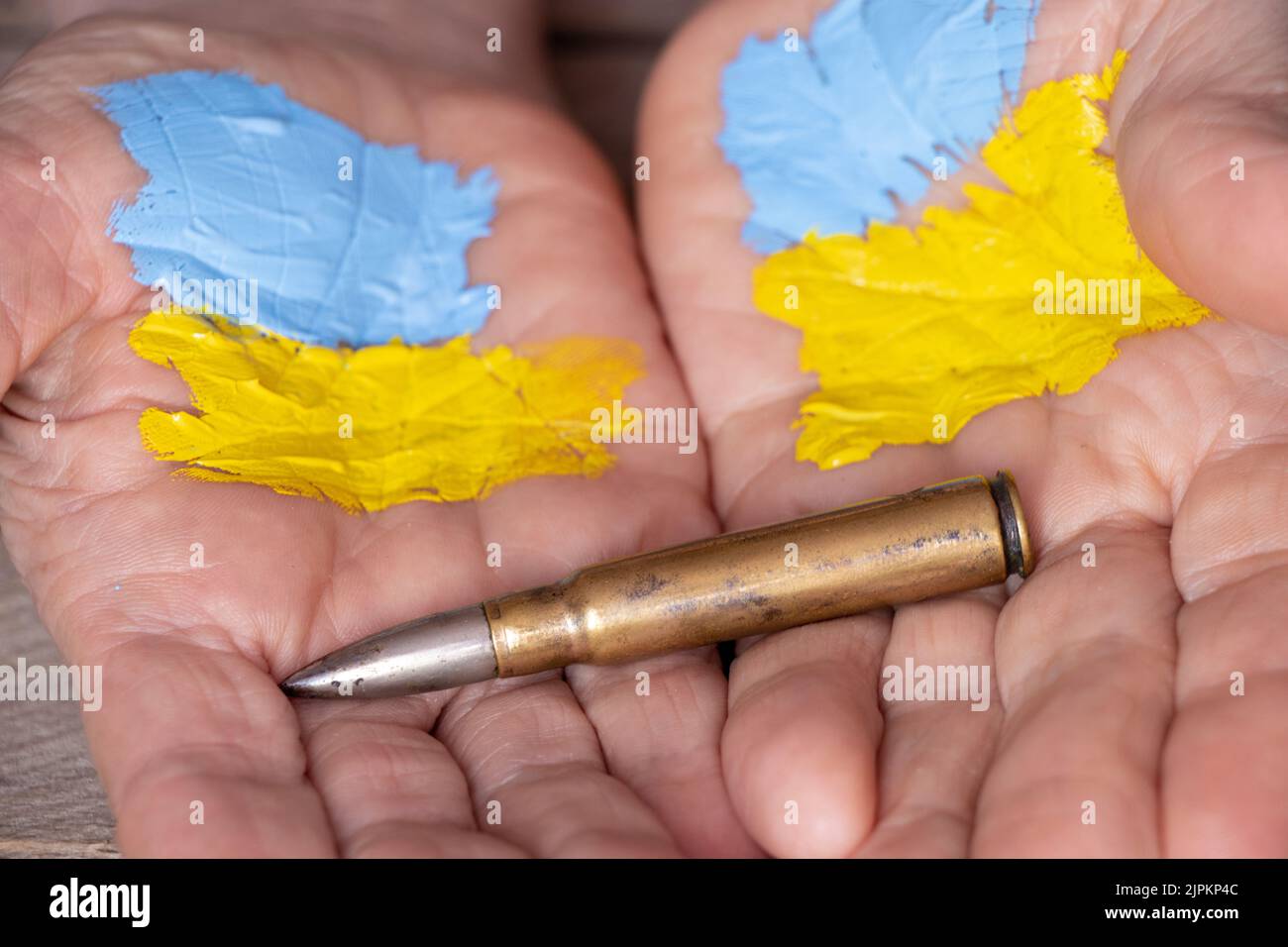 Le mani di una vecchia donna con una bandiera dipinta dell'Ucraina detengono una pallottola militare su uno sfondo di legno, guerra in Ucraina, donna militare Foto Stock