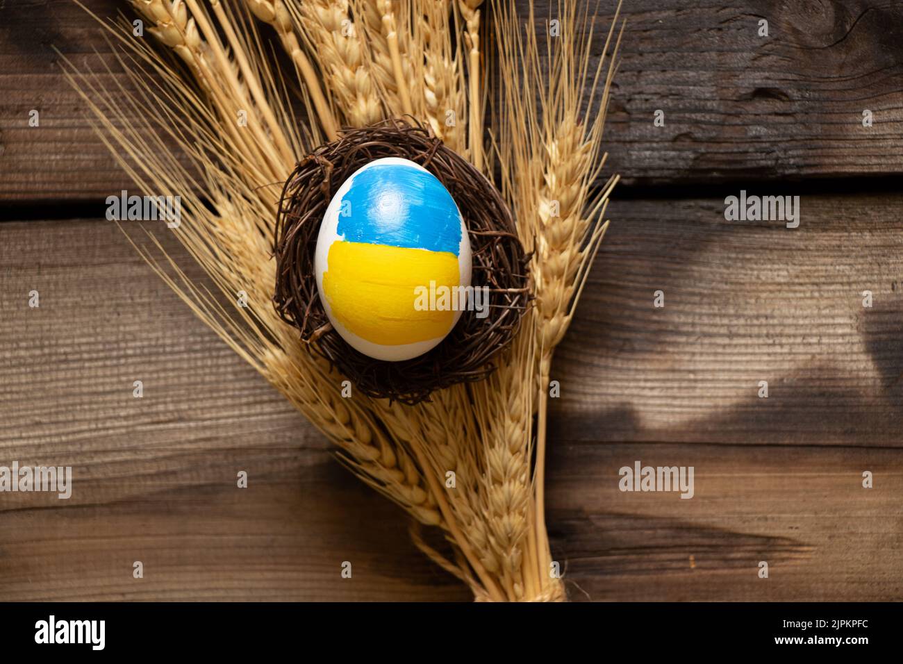 Un uovo di pollo bianco con una bandiera dipinta di Ucraina in un cesto di paglia è sulle orecchie di grano, cultura e vacanze 2022, raccolto in Ucraina Foto Stock