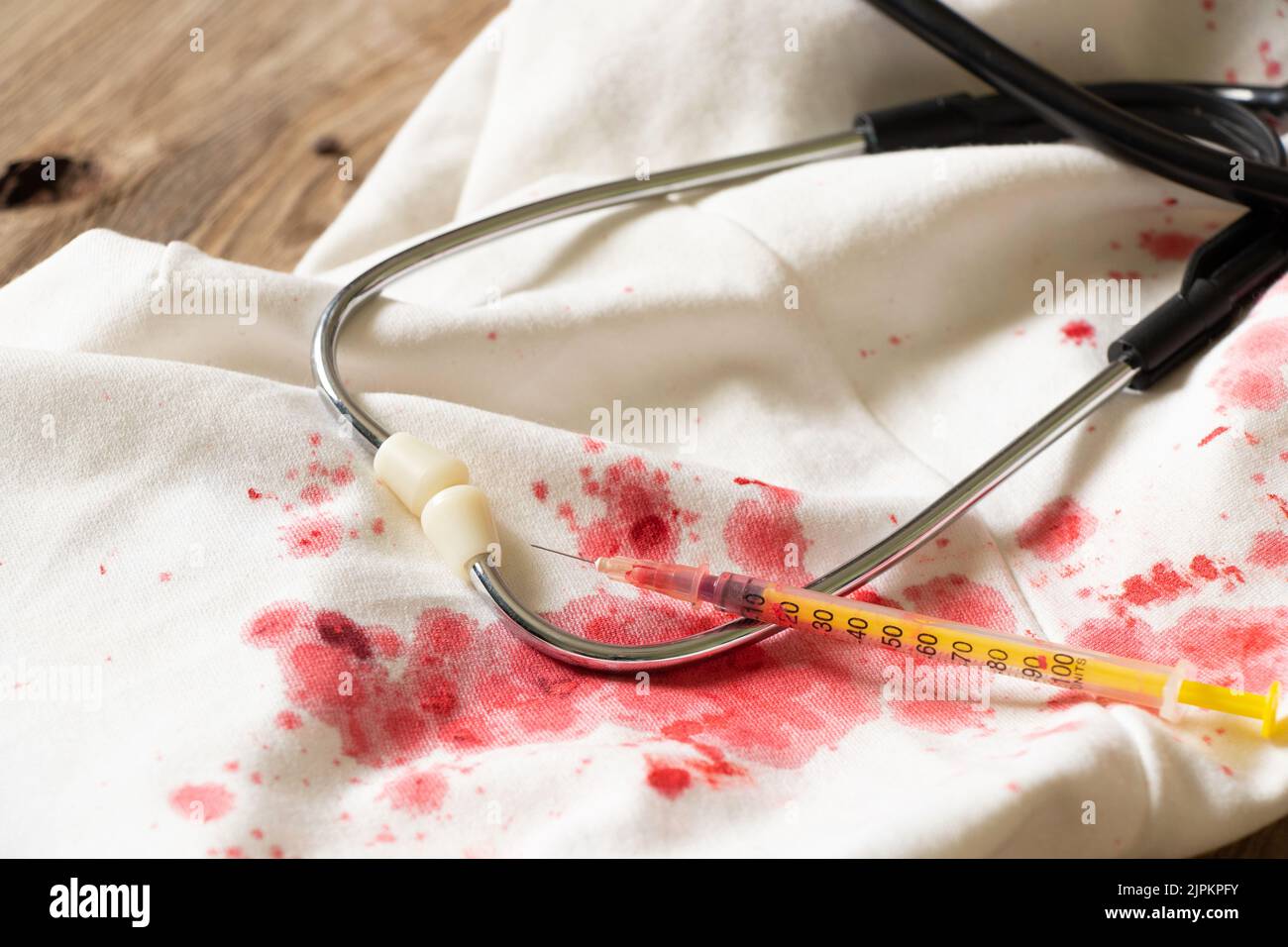 Uno stetoscopio e una siringa giacciono su un vestito bianco con macchie di sangue rosso, tracce di sangue sulle cose e apparecchiature mediche, cure mediche Foto Stock