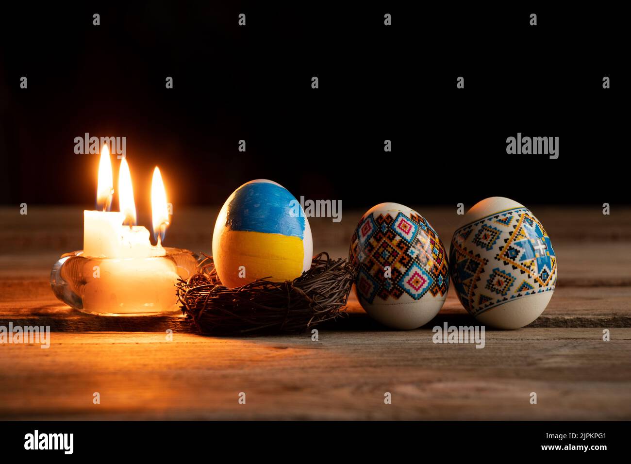 Colorante uovo di pollo con una bandiera dipinta di Ucraina e una fiamma di candela sul tavolo a casa in Ucraina al buio, vacanze di Pasqua in Ucraina durante la wa Foto Stock