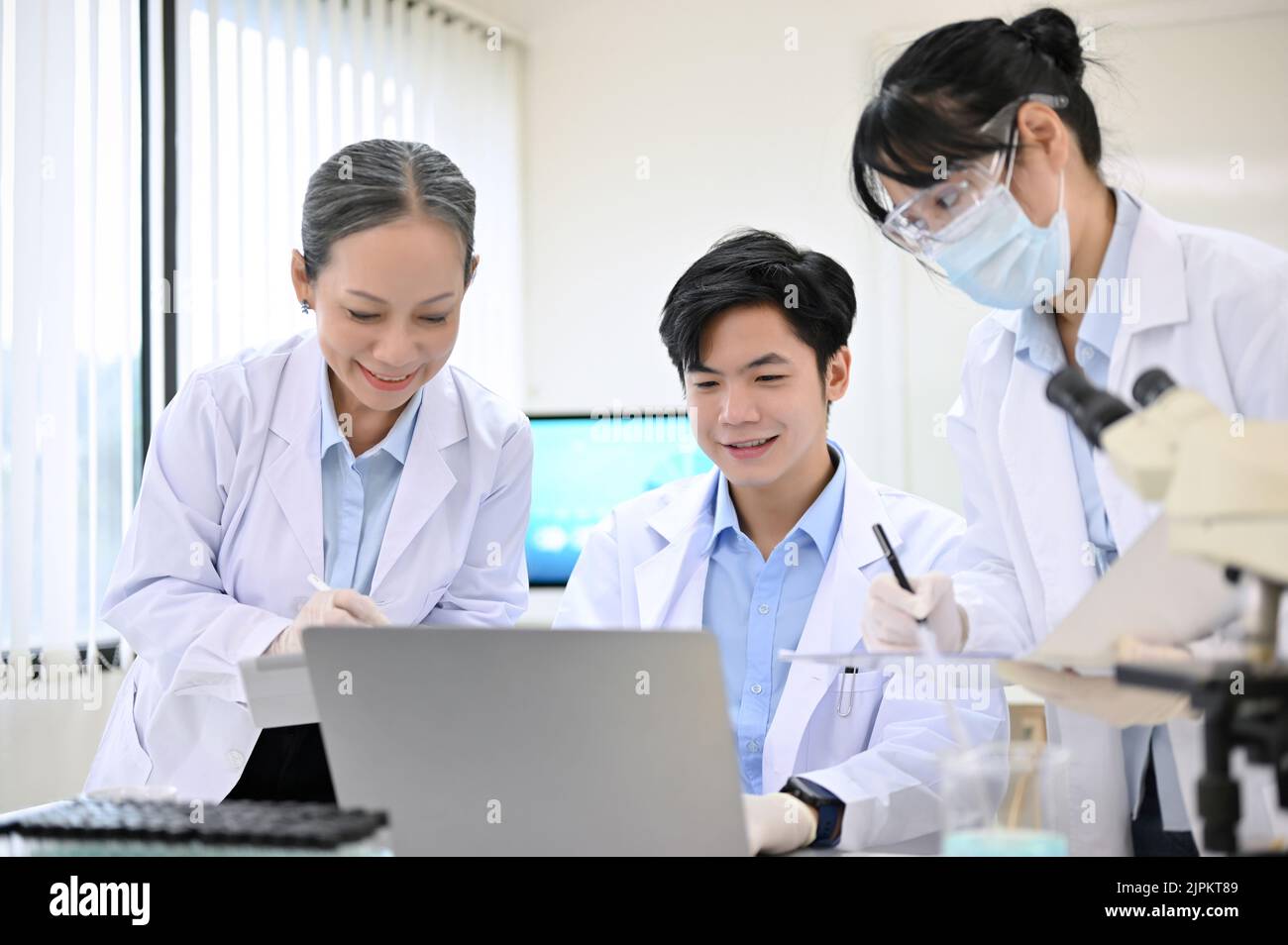 Gruppo di uno scienziato asiatico o di un tecnico medico in abito bianco guardando il risultato dell'esperimento nello schermo del portatile insieme nel laboratorio. Foto Stock