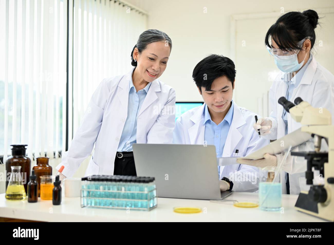 Un team di allegri e professionisti scienziati asiatici stanno lavorando insieme in laboratorio, controllando i risultati sperimentali sul computer portatile. Lavoro di squadra c Foto Stock