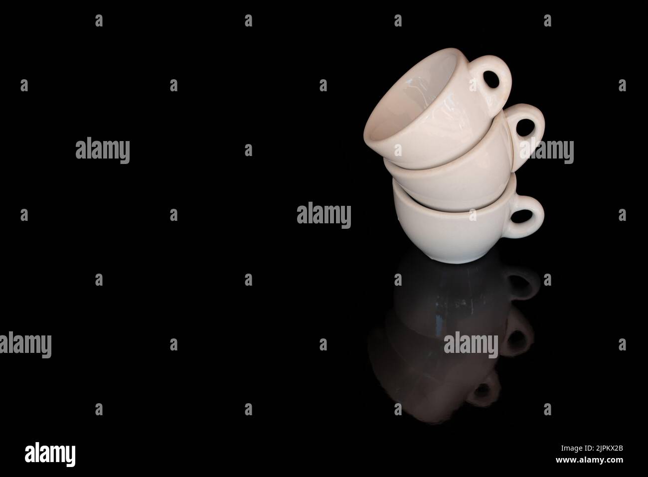 Tre vecchie tazze da caffè bianche sono impilate sul bordo. Lo sfondo è nero. Le tazze si riflettono sul terreno. C'è spazio per il testo. Foto Stock