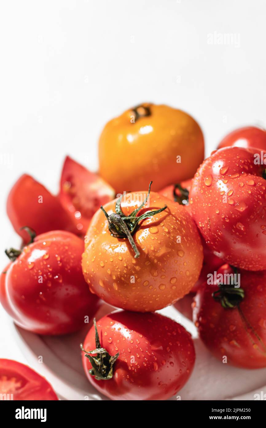 Pomodori freschi e colorati (rosso, giallo, arancione) su piatto bianco con ombre dure su sfondo testurizzato Foto Stock