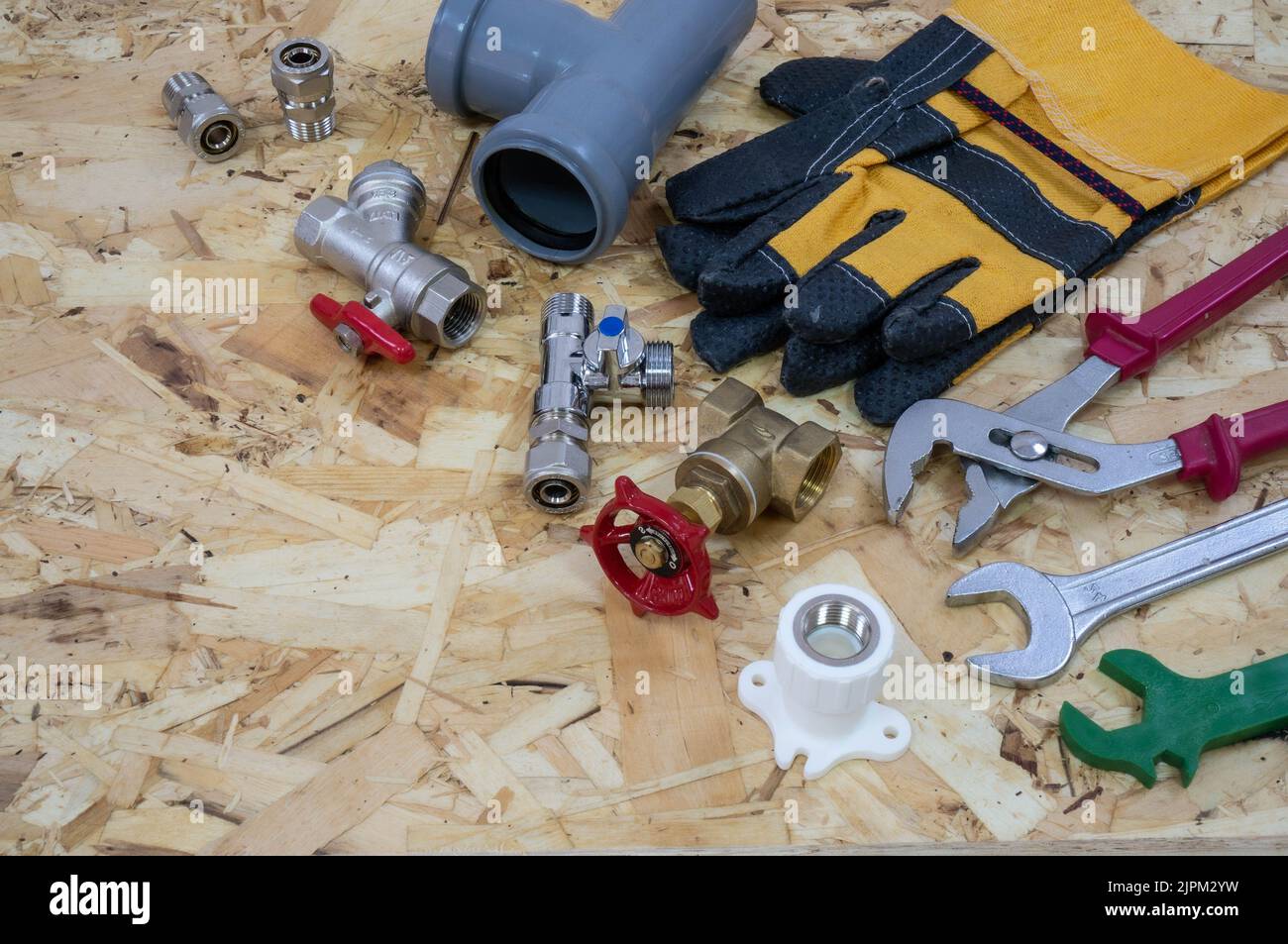 Utensili idraulici, parti, componenti di tubazioni e guanti sullo sfondo di una piastra OSB per edilizia. Posizionare il testo o il logo nell'angolo sinistro. Foto Stock