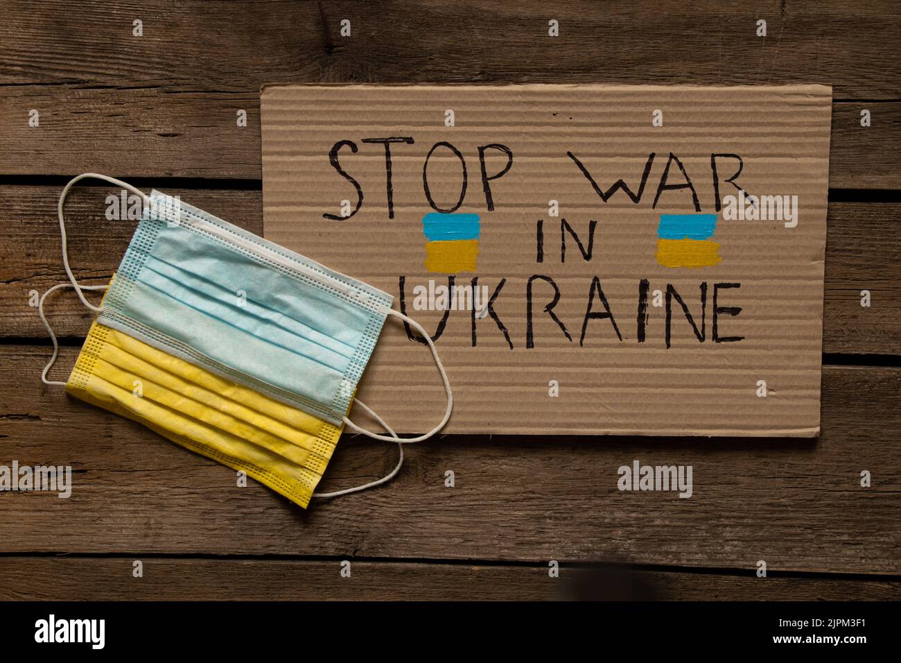 Maschere mediche, giallo e blu, come la bandiera dell'Ucraina, giacciono su un tavolo di legno e un segno con il testo fermare la guerra in Ucraina. Bandiera dello Stato di Ukrain Foto Stock