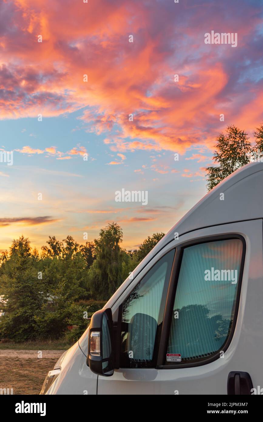 Nuvole colorate e cielo durante il tramonto con camper davanti e colori rosso arancio e blu Foto Stock