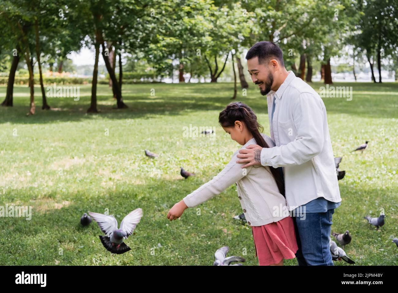 Papà asiatico che abbraccia la figlia vicino agli uccelli nel parco estivo Foto Stock