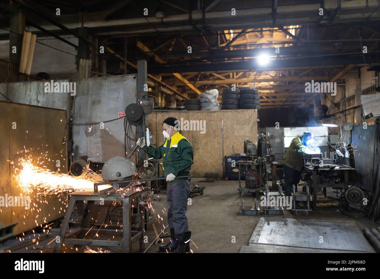 Lavoratori che lavorano con la costruzione di metallo su stabilimento. Lavorazione del metallo con sega a disco per smerigliatrice ad angolo grande e saldatura a saldatrice. Scintille nella lavorazione dei metalli in fabbrica. Foto Stock