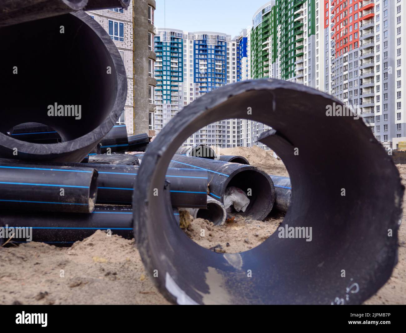 Vista attraverso un enorme tubo nero sopra il sito dell'edificio con nuovi alti edifici sullo sfondo a Kyiv, Ucraina. Nuovo distretto in costruzione Foto Stock