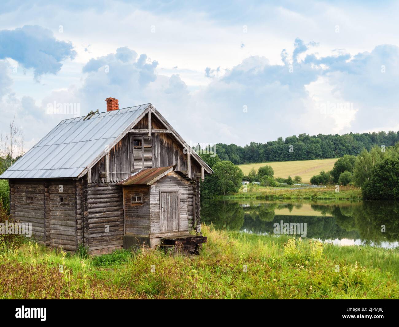 vecchia cabina in legno vicino al fiume sotto le nuvole grigie il giorno d'estate Foto Stock