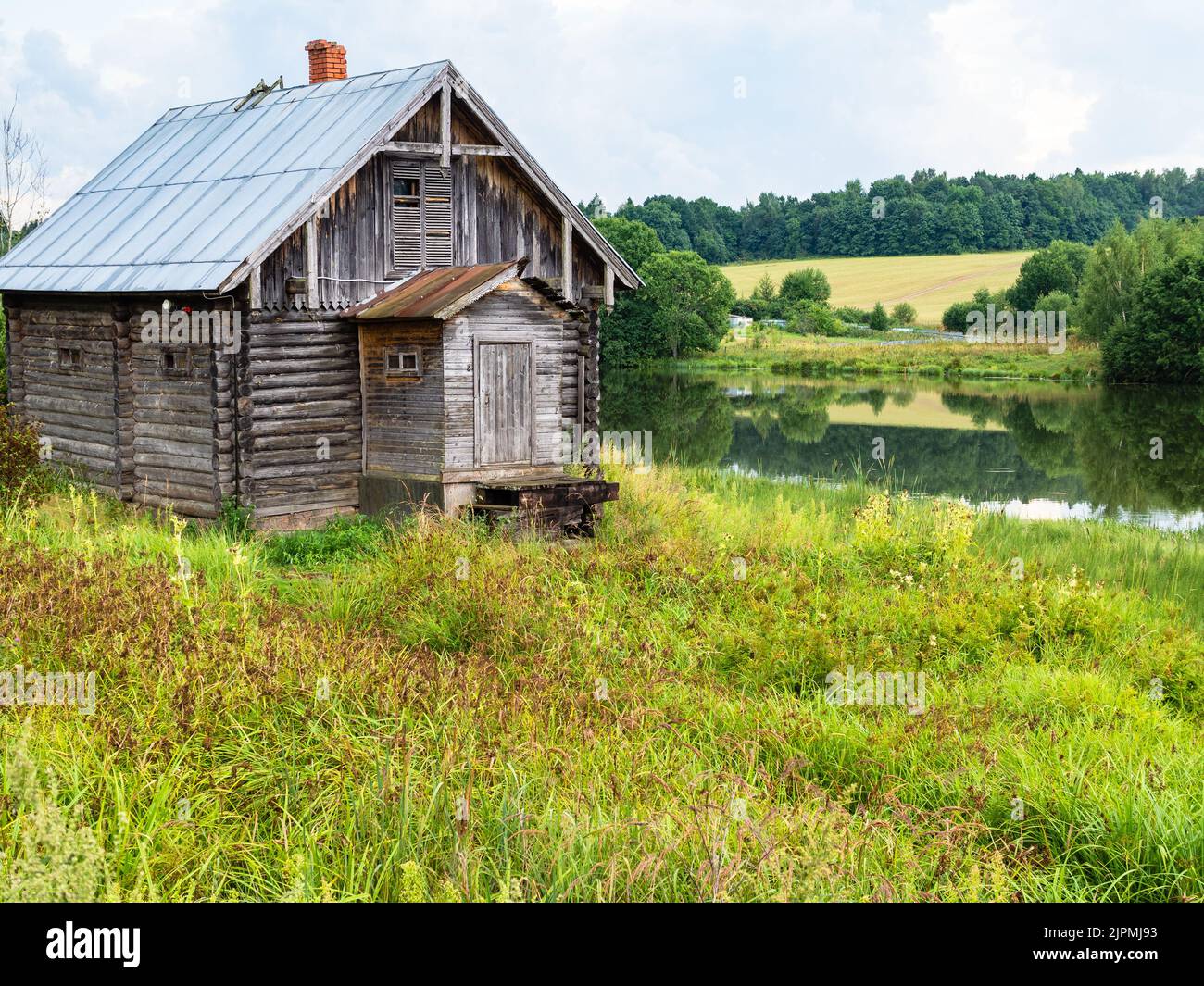 vecchia cabina in legno sulla riva del fiume troppo coltivata dopo la pioggia il giorno d'estate Foto Stock