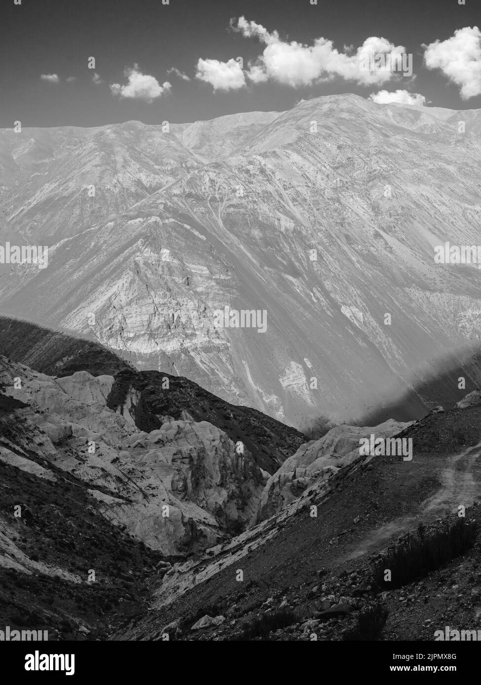 Vista attraverso la valle di Spiti con alte creste e ripide pendici delle montagne Himalaya sotto il cielo blu brillante con le nuvole durante l'estate vicino a Kaza, India. Foto Stock