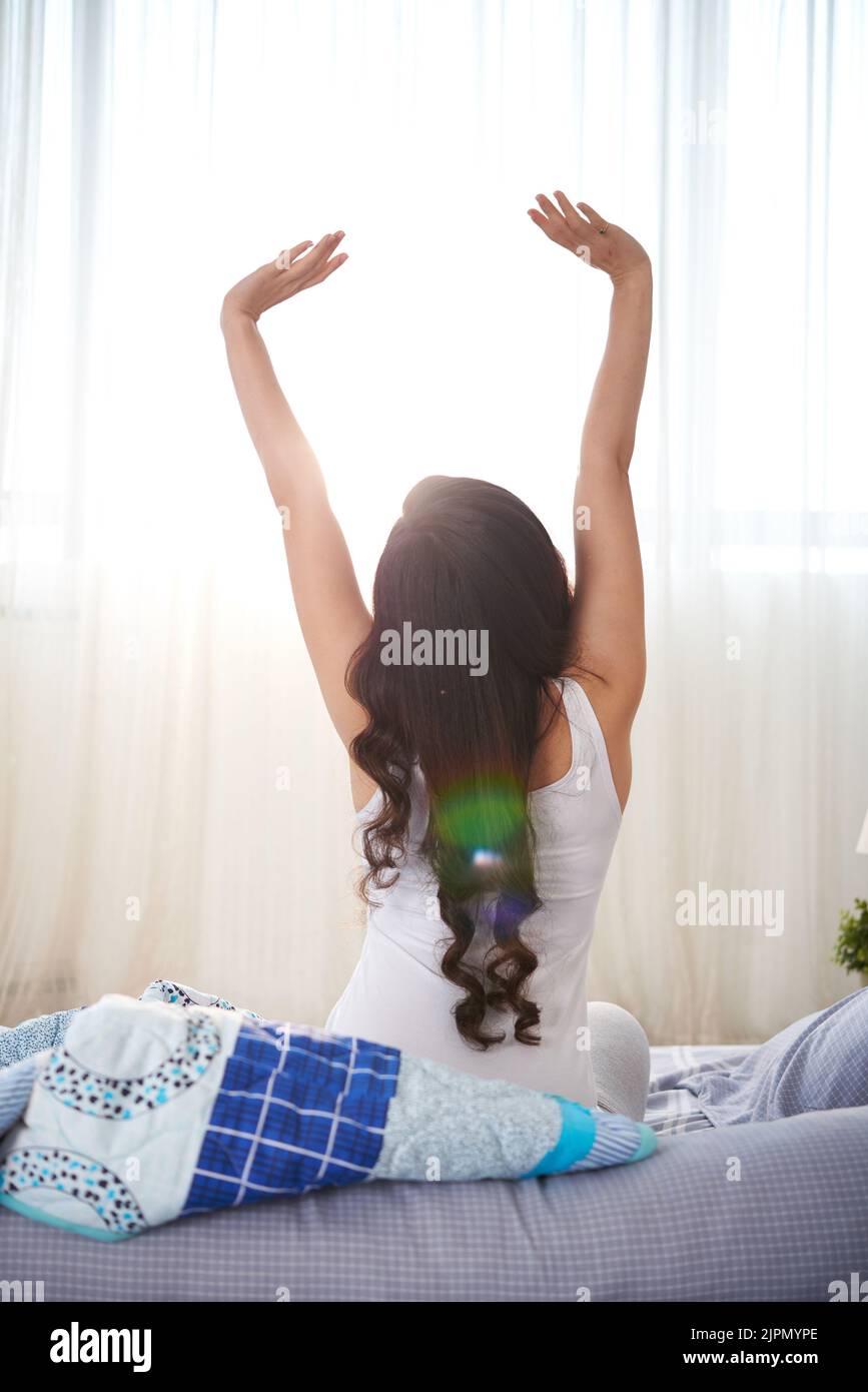 Giovane donna con lunghi capelli ricci che si allungano al mattino, vista dal retro Foto Stock