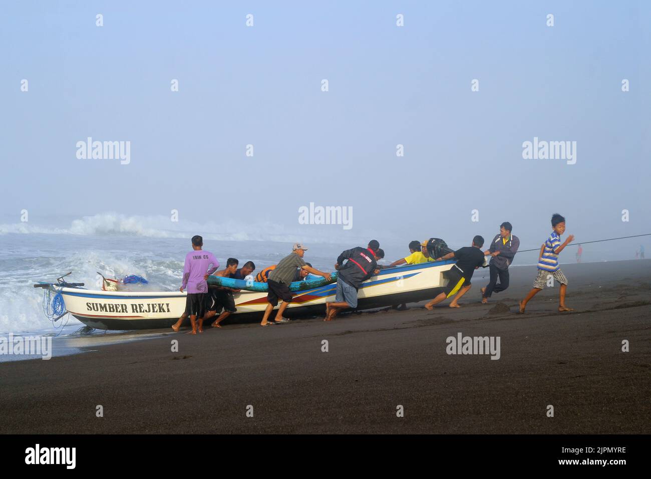 Una vista di alcune persone che aiutano a tirare le barche da pesca alla spiaggia Foto Stock