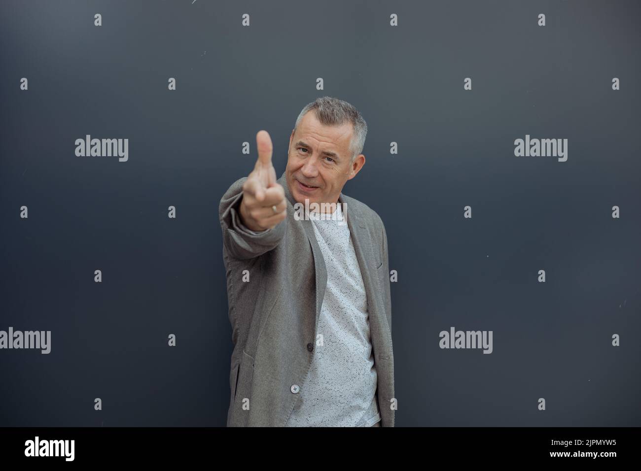 Ritratto di uomo d'affari anziano carino in piedi su sfondo grigio, puntando il dito indice verso la macchina fotografica. Stile di vita attivo. Foto Stock