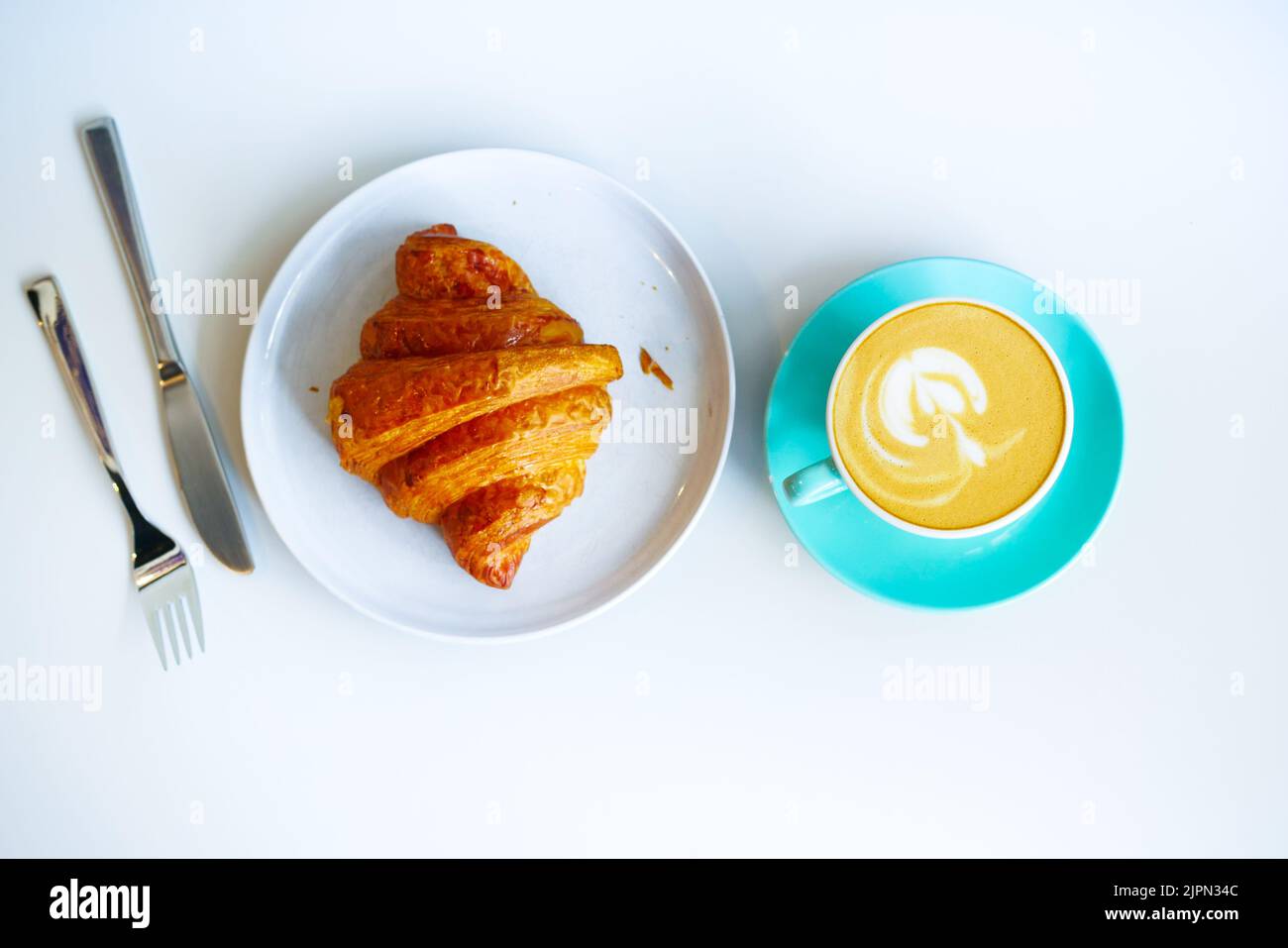 Una tazza di caffè tardivo dal design floreale sulla parte superiore e croissant sul bianco Foto Stock