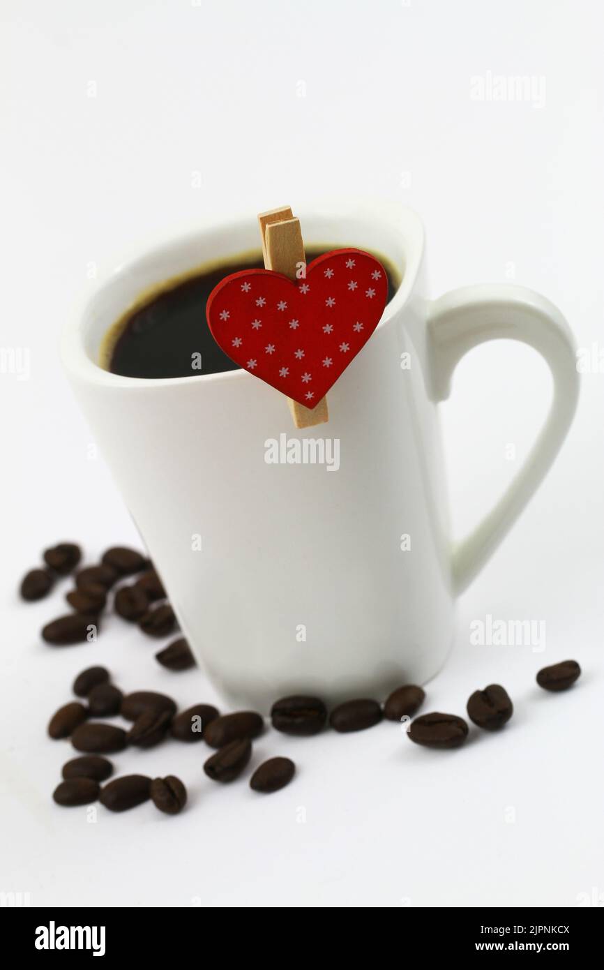Clip in legno con cuore rosso punteggiato sulla parte superiore della tazza di caffè bianca con chicchi di caffè sparsi e spazio per le copie Foto Stock