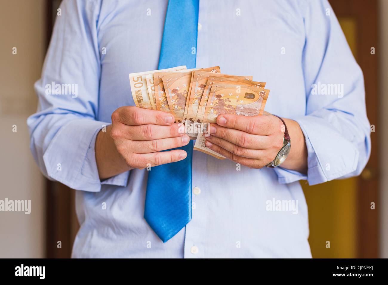Primo piano delle mani di un uomo caucasico irriconoscibile in possesso di diversi banconote da 50 euro. La persona è vestita con una camicia blu e una cravatta blu, indossando un Foto Stock