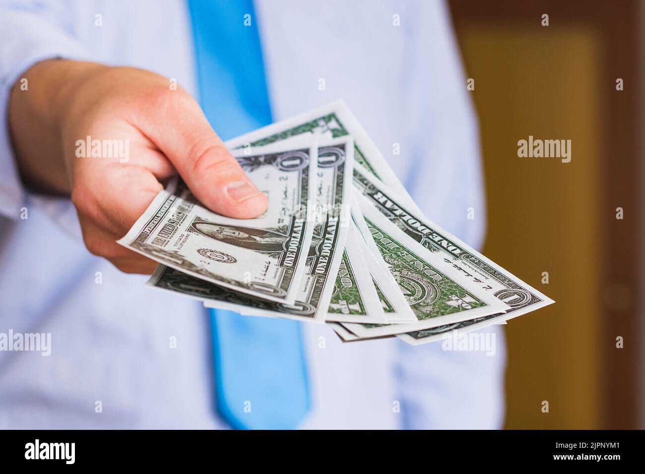 Primo piano della mano di un uomo caucasico irriconoscibile in possesso di diverse banconote in dollari USA. La persona è vestita con una camicia blu e cravatta blu, weari Foto Stock