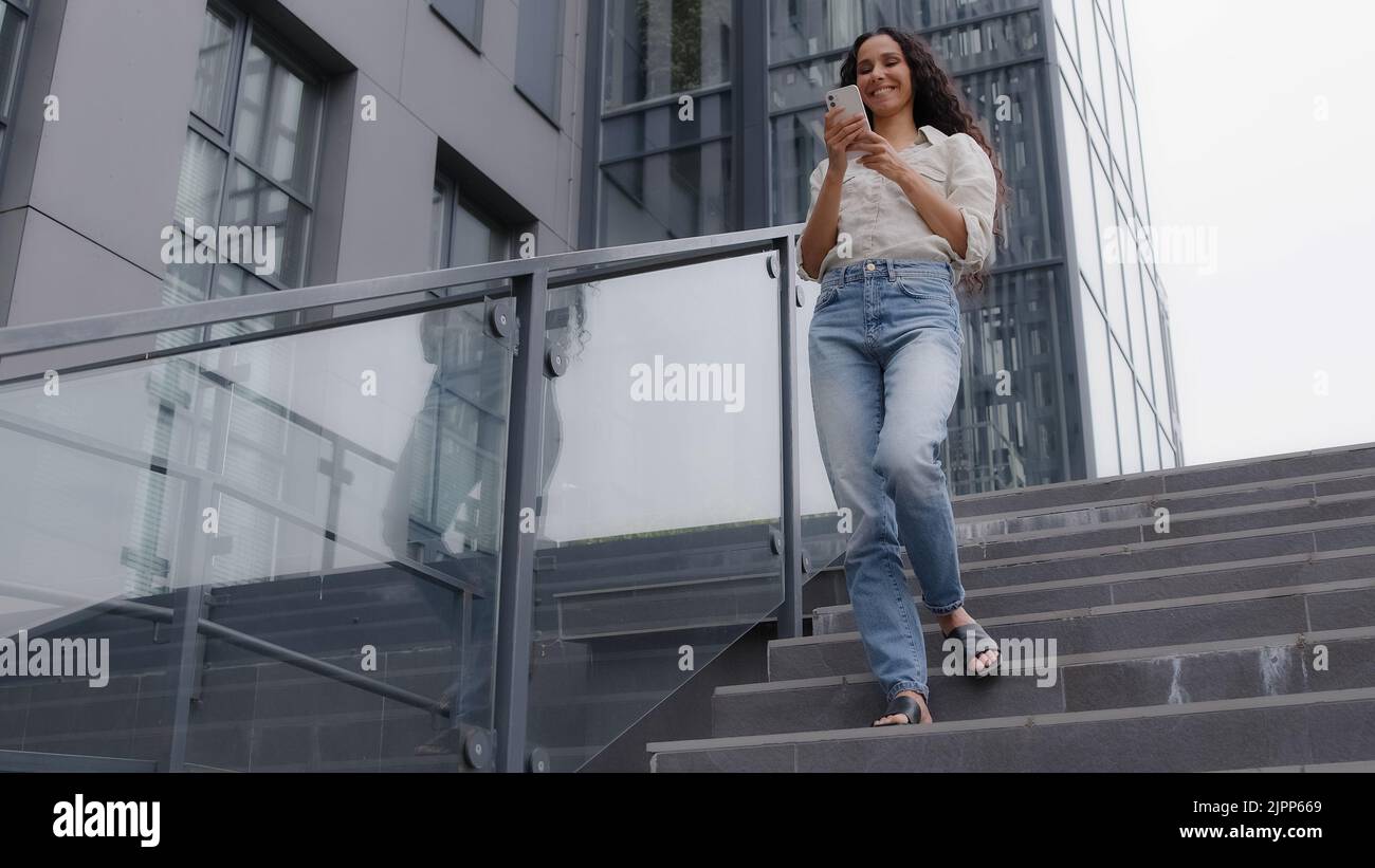 Donna 30s slim donna in jeans e camicia in piedi in città vicino alla costruzione azienda guardando telefono cellulare schermo chatting mobile data app. Donna d'affari caucasica Foto Stock
