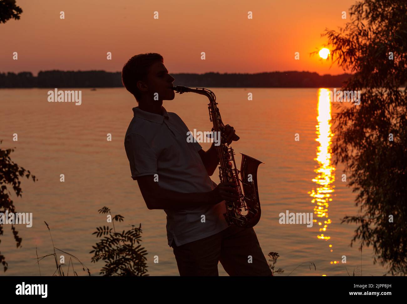 Un giovane suona il sassofono la sera al tramonto. Foto Stock