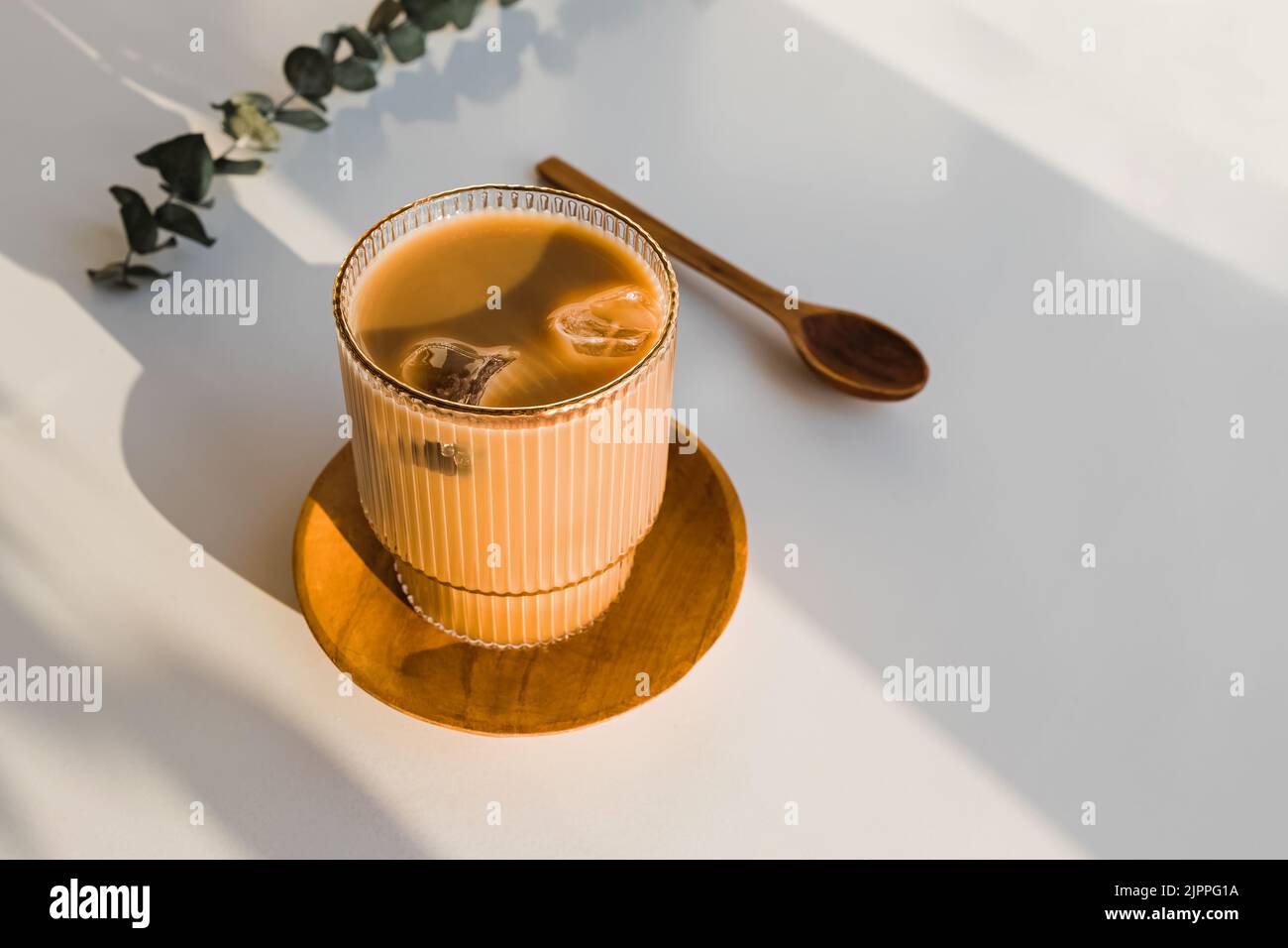 Caffè con ghiaccio in un vetro di cristallo sul tavolo bianco in luce naturale, ombre lunghe Foto Stock