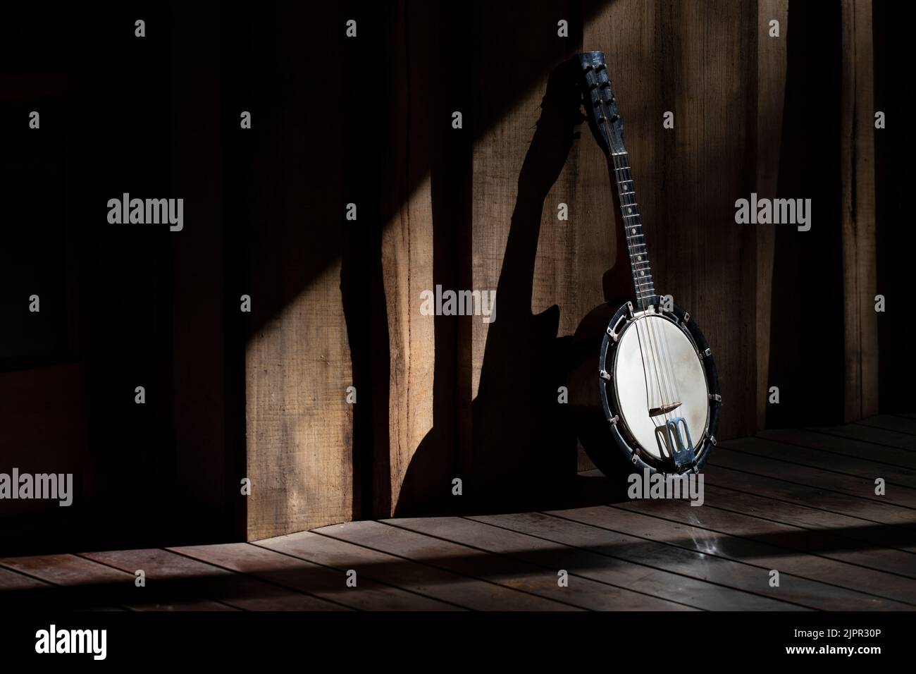 Mandolin Banjo classico, su una veranda in legno con luce solare che crea un contrasto drammatico di luce moody e forti ombre. Spazio di copia. Foto Stock