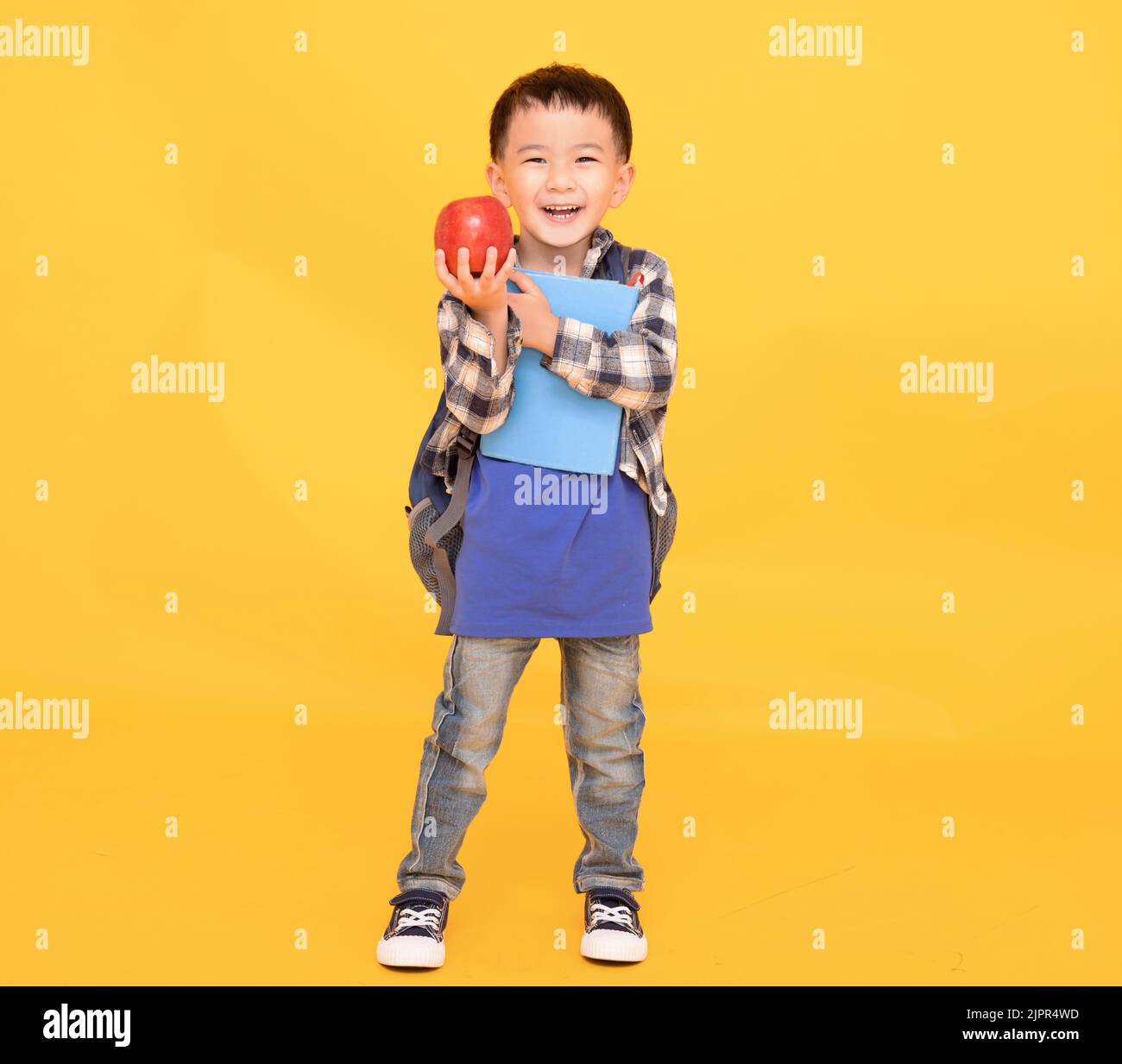 Bambino della scuola con lo zaino tenere mela e libro isolato sul giallo Foto Stock