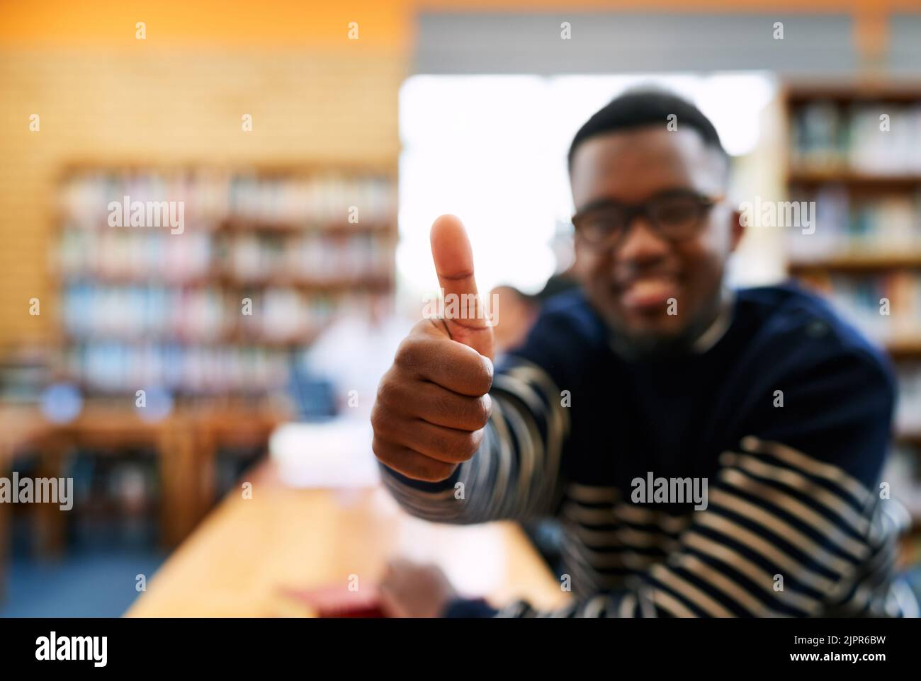 Sentirsi positivi per il mio futuro. Ritratto ritagliato di uno studente che mostra i pollici in su mentre si siede in biblioteca. Foto Stock