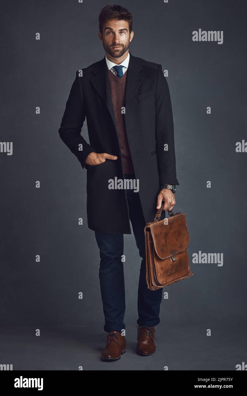 Mettere al lavoro il suo stile. Studio ritratto di un giovane uomo elegantemente vestito che porta una borsa su uno sfondo grigio. Foto Stock