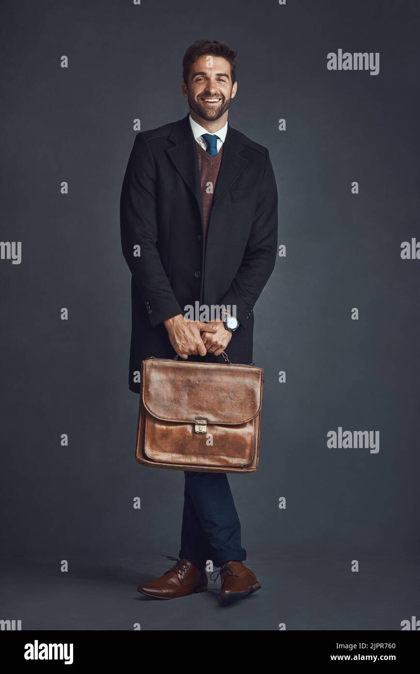 Pronto per qualsiasi cosa con questo stile. Studio ritratto di un giovane uomo elegantemente vestito che porta una borsa su uno sfondo grigio. Foto Stock