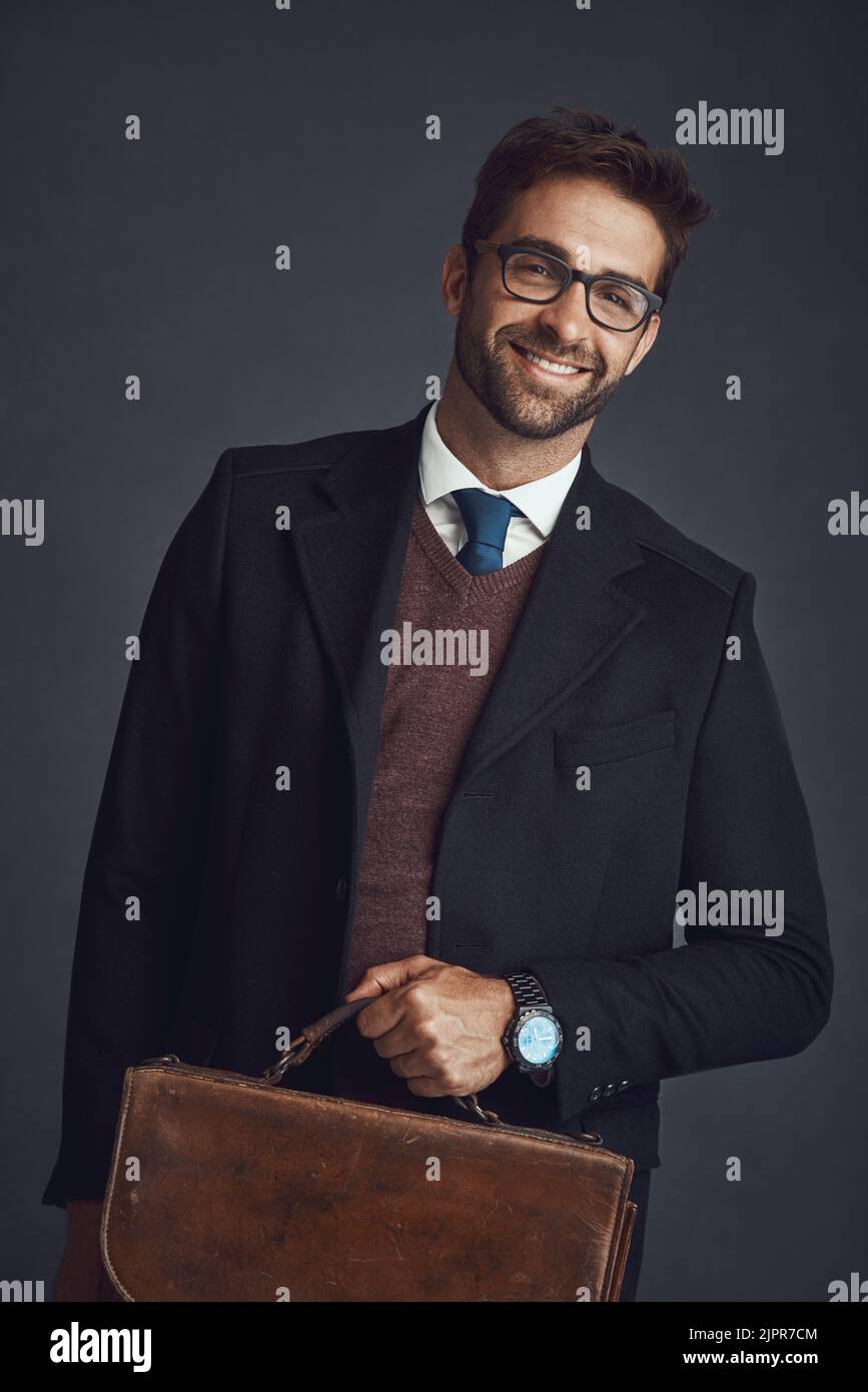 L'uomo dell'ora. Studio ritratto di un giovane uomo elegantemente vestito che porta una borsa su uno sfondo grigio. Foto Stock