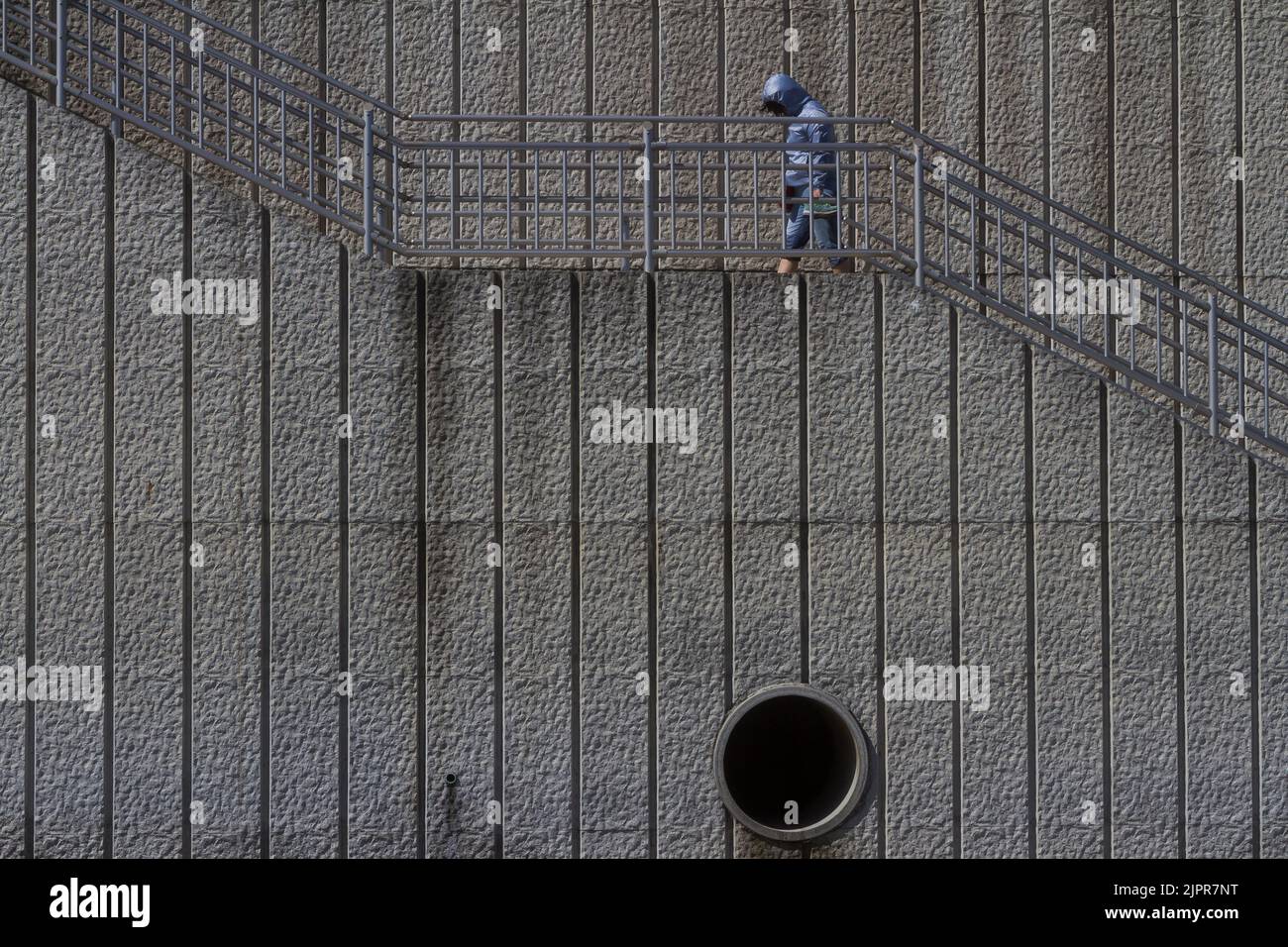 Una persona che indossa una giacca a vento sale le scale in un muro di mare a Kamakura Beach, Kanagawa, Giappone. Foto Stock
