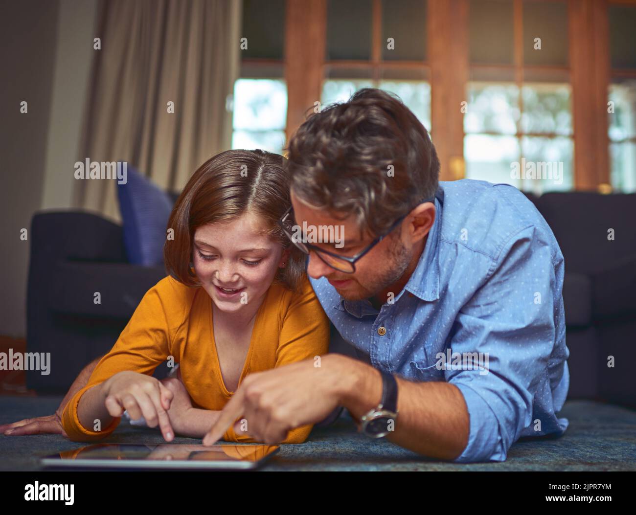 Imparare a conoscere la sicurezza online. Un padre e una figlia sdraiati sul pavimento e che utilizzano un tablet digitale insieme a casa. Foto Stock