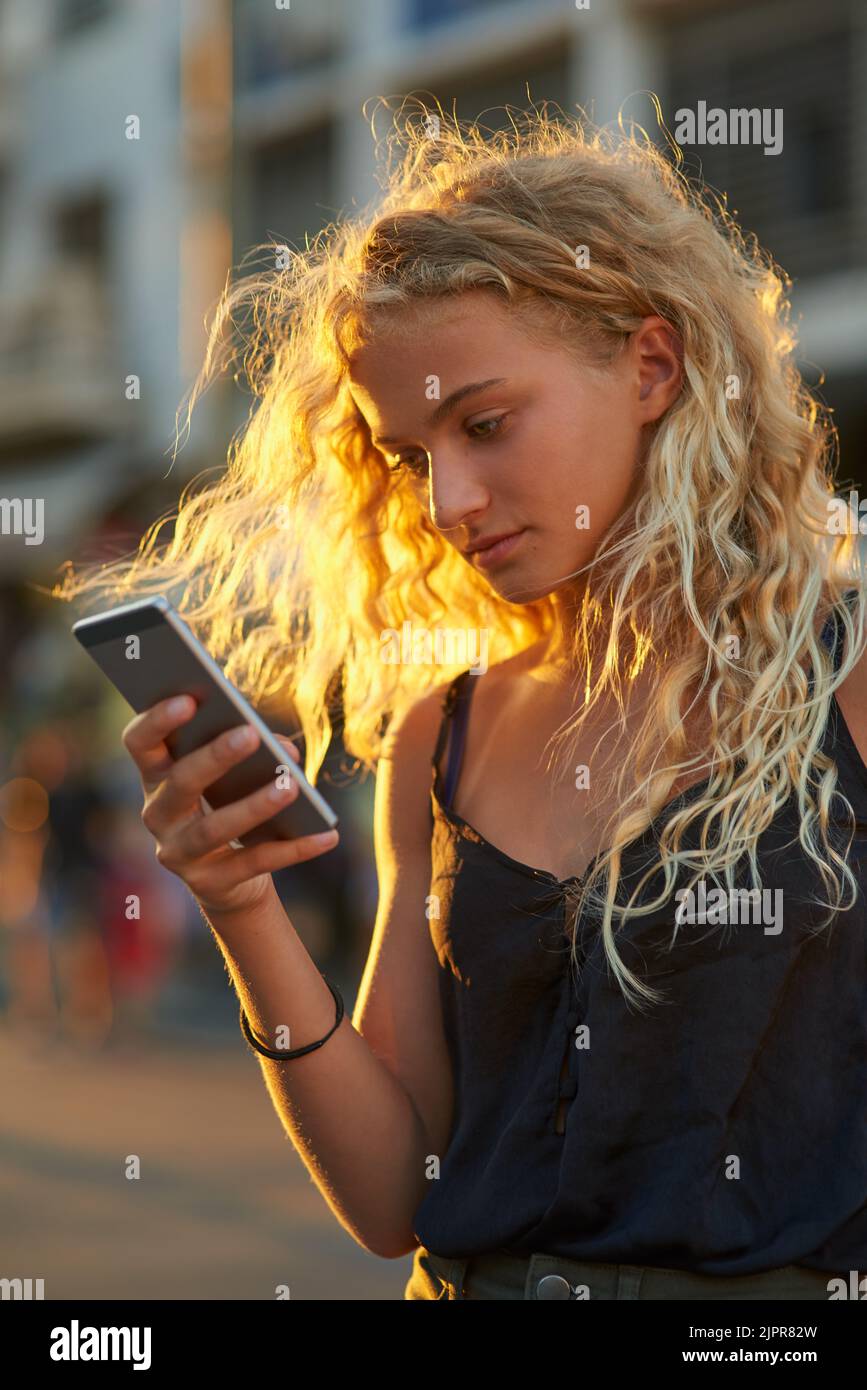 Controllare i suoi messaggi. Una giovane donna attraente che invia un testo mentre cammina per la città. Foto Stock