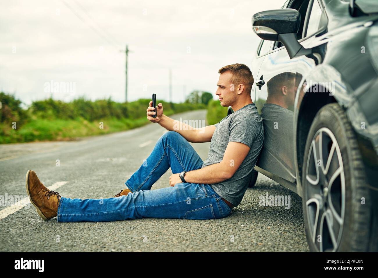 In attesa che le ruote siano trainate via, un giovane uomo in attesa di assistenza stradale dopo la rottura. Foto Stock