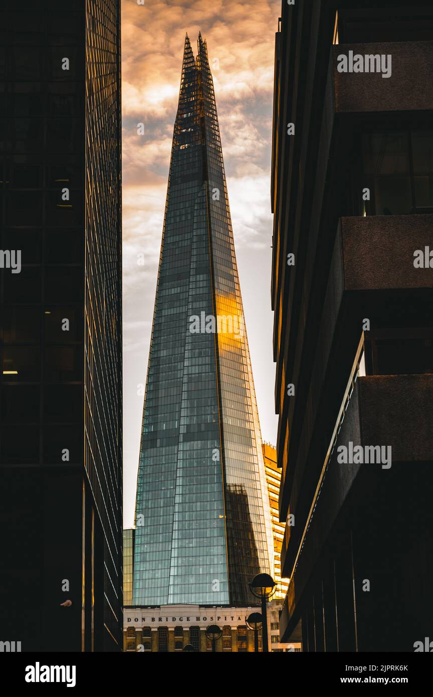 Uno scatto verticale del grattacielo Shard tra gli edifici degli uffici al tramonto con cielo nuvoloso a Londra Foto Stock
