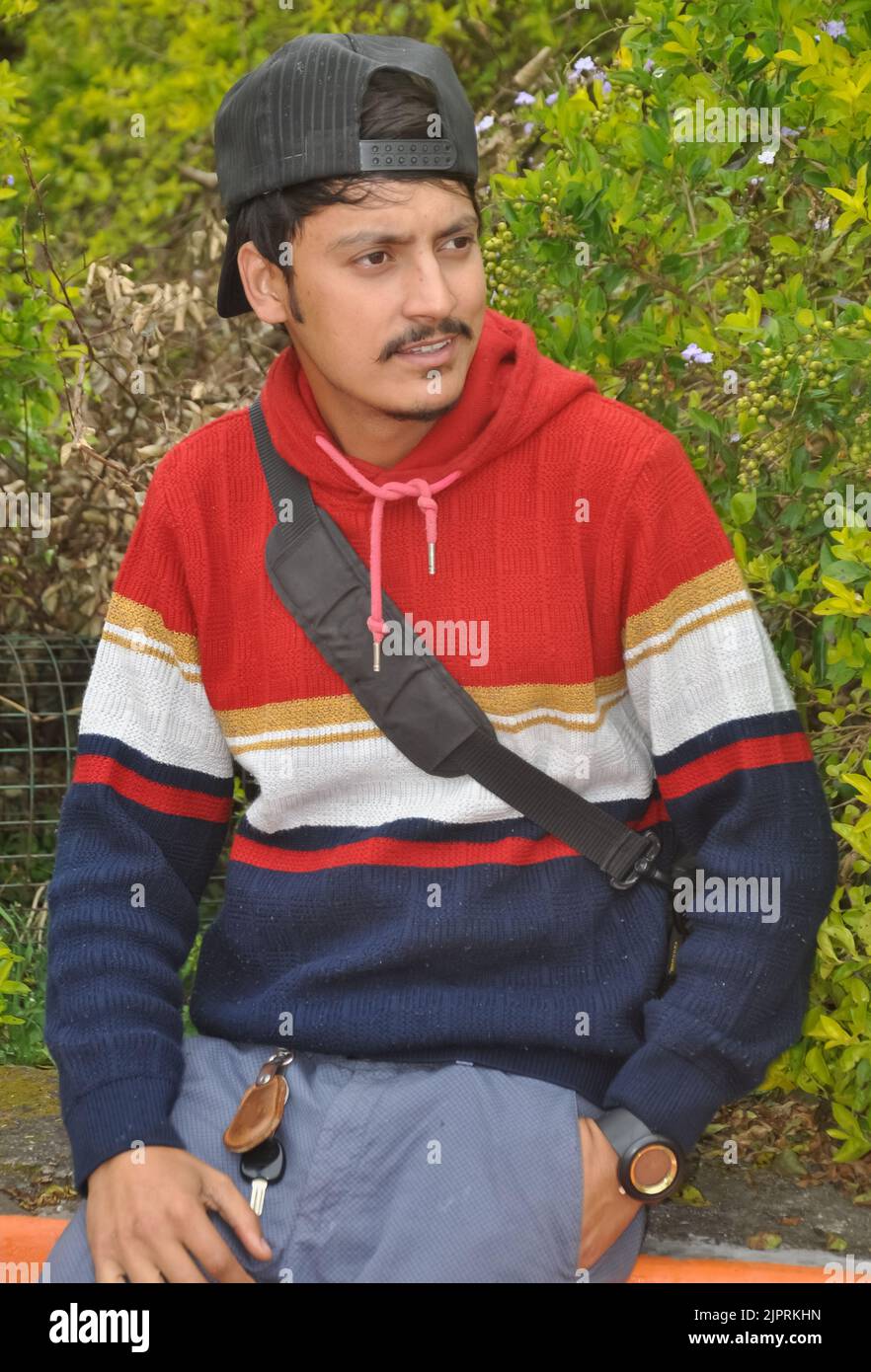 Un giovane ragazzo indiano bello che indossa il cappuccio all'indietro con guardare lateralmente mentre si siede all'aperto Foto Stock
