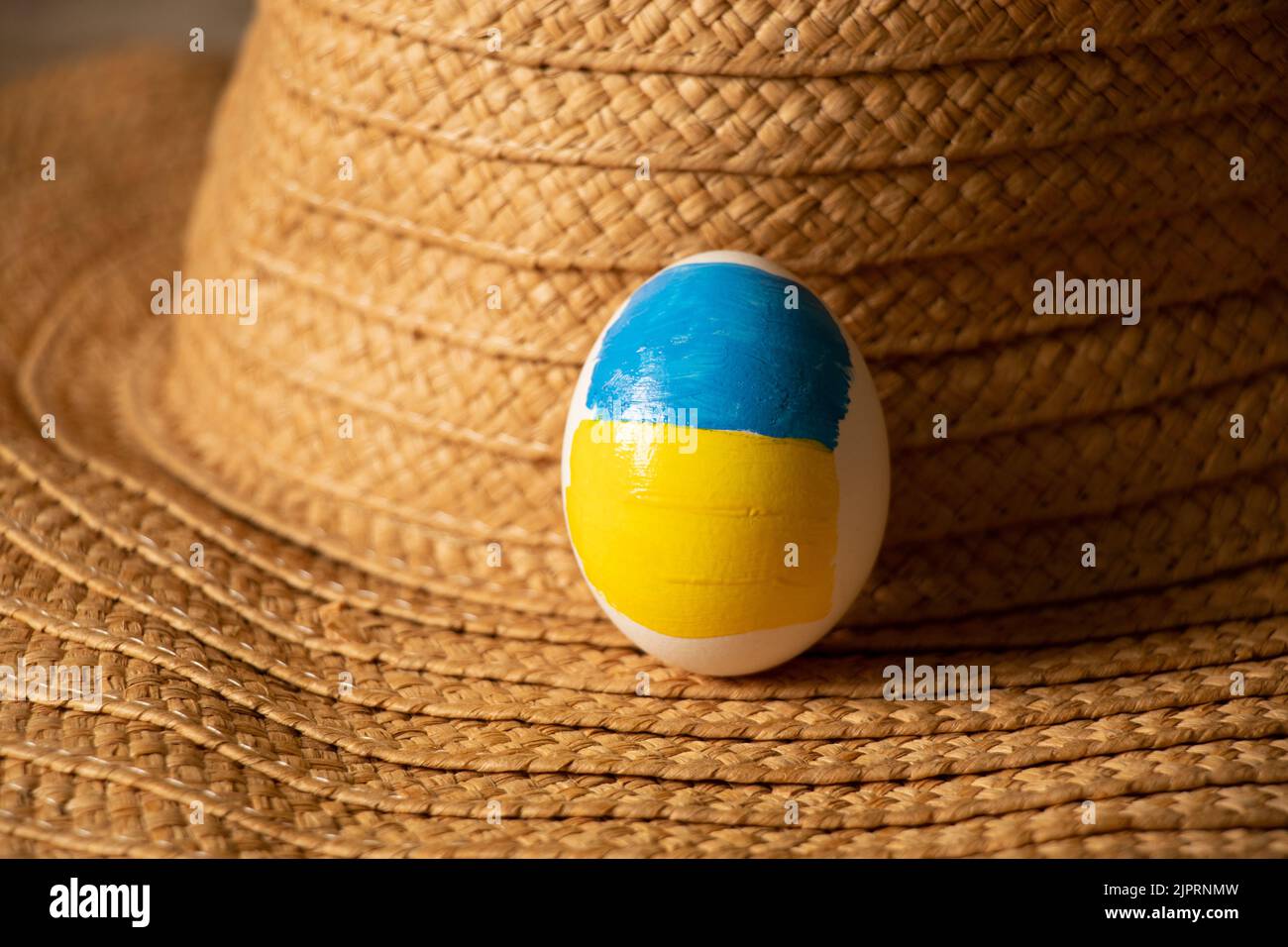 Un uovo di pollo bianco con una bandiera dipinta di Ucraina si trova su un cappello di paglia sul tavolo a casa, la cultura e le vacanze 2022 Foto Stock