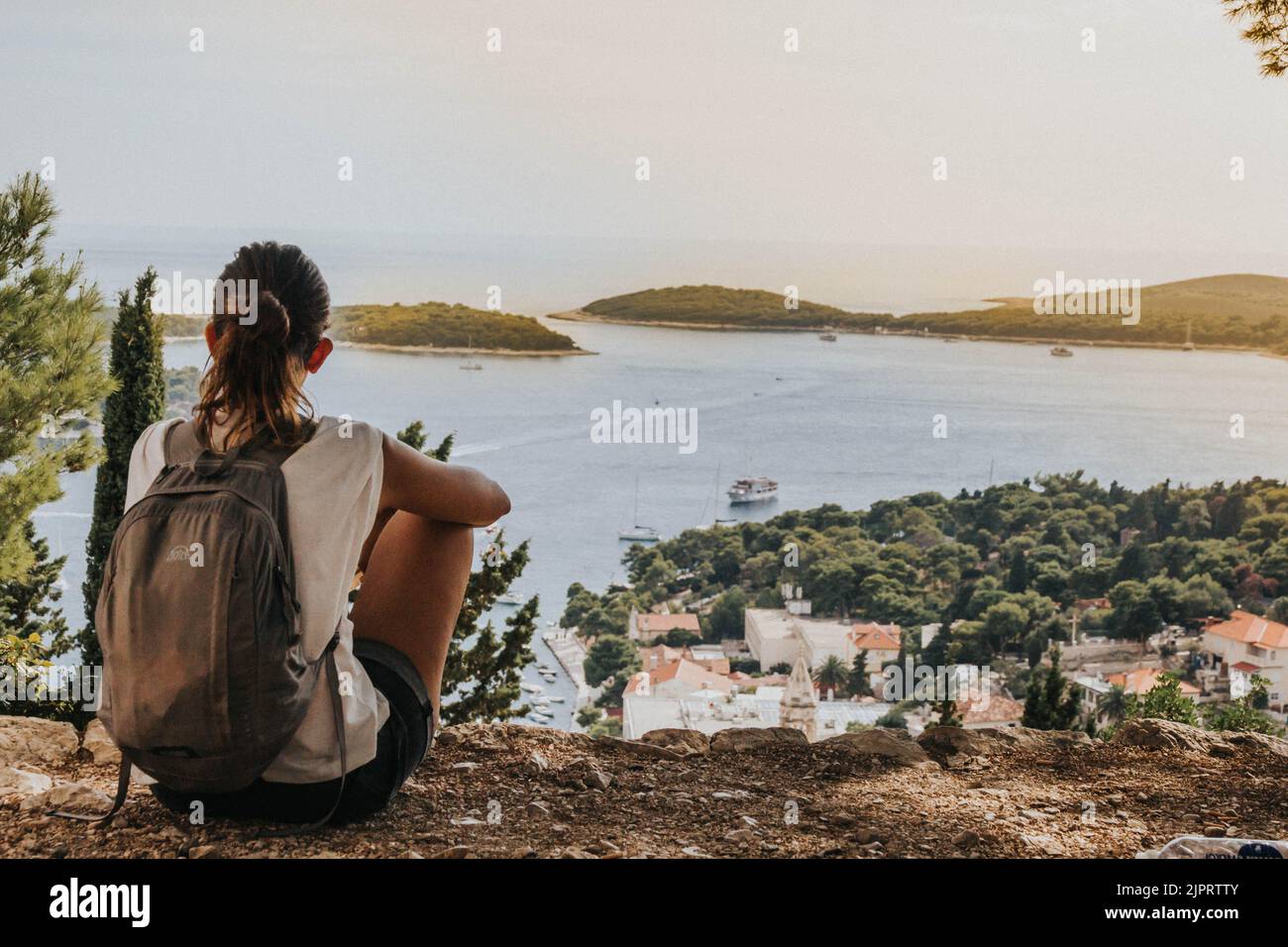 Una vista posteriore di una bella donna seduta sul terreno e guardando Hvar in Croazia Foto Stock