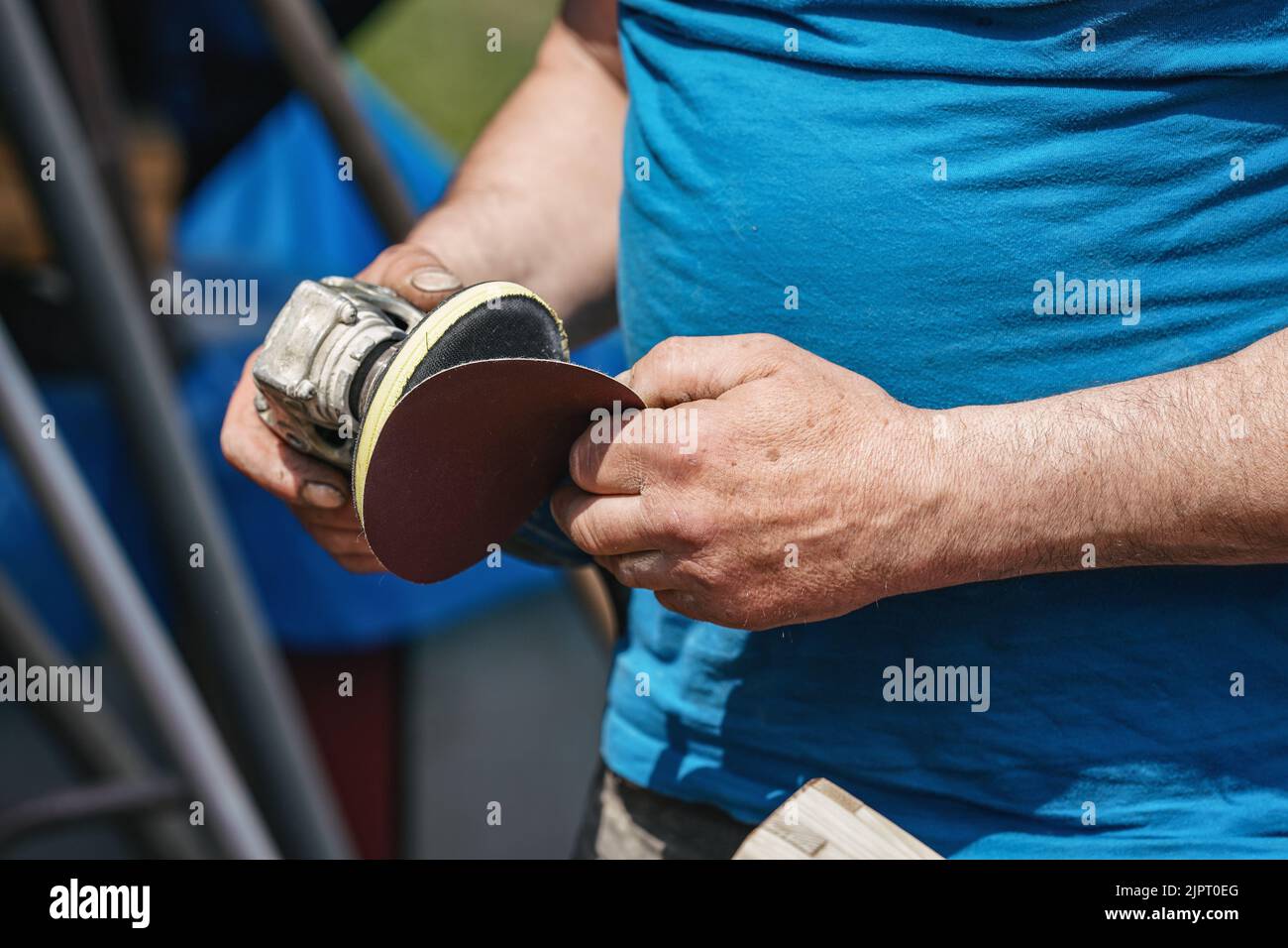 Uomo che mette nuova carta vetrata sulla smerigliatrice rotante, dettaglio solo sulle sue mani Foto Stock
