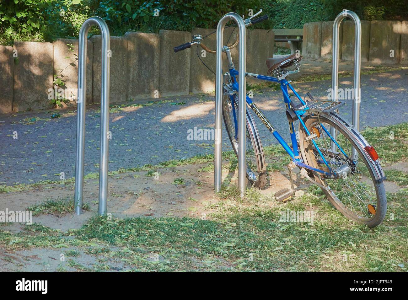 Una bicicletta blu parcheggiata nel parco in Germania con alberi verdi sullo sfondo Foto Stock
